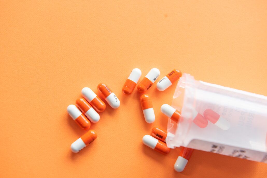 Nezaťažujte imunitu - na imunitu môže mať vplyv aj užívanie niektorých liekov. Kapsule liekov hodené na oranžový podklad.