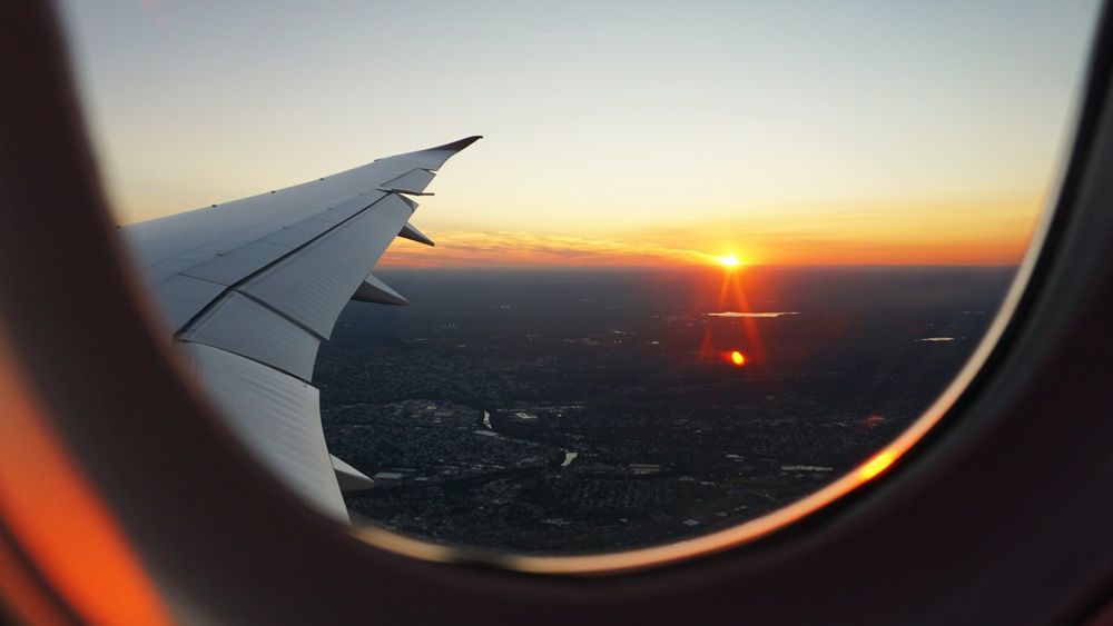 Výhľad z okna lietadla na jeho krídlo a západ slnka