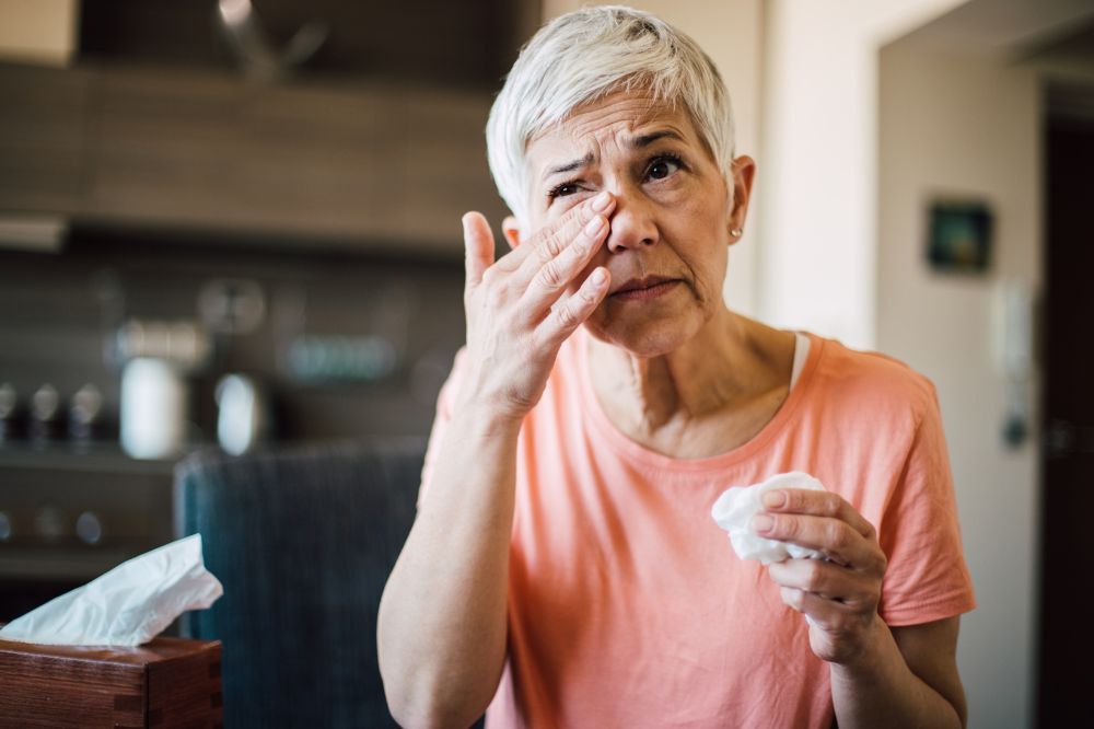Staršia žena drží v ruke vreckovku a utiera si oko, pretože jej slzia z dôvodu podráždenia a zápalu oka.