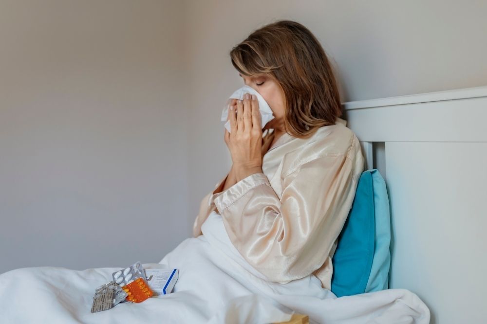 Selén podporuje správnu funkciu imunitného systému. Žena s nádchou leží v posteli a fúka si nos.