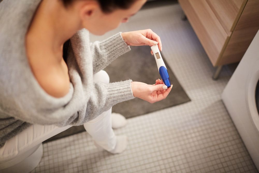 Žena sedí v kúpeľni a pozerá sa na tehotenský test, pretože v dôsledku poruchy štítnej žľazy má problémy s plodnosťou.
