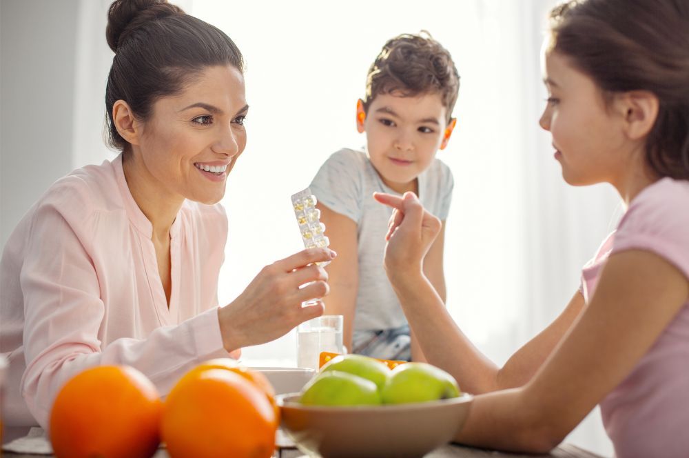 Mama sa usmieva dáva svojím deťom vitamíny, ktoré sú určené pre deti, aby mali podporenú imunitu a zdravo rástli. 