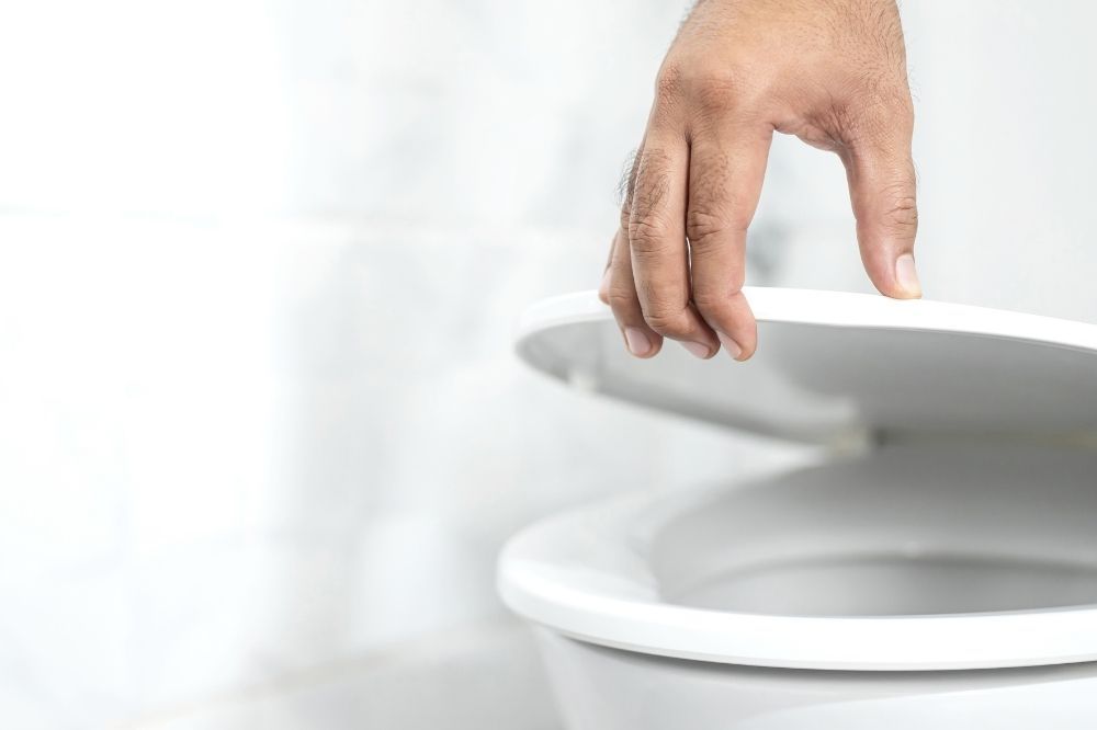 Príznaky zväčšenej prostaty. Záber na ruku dvíhajúcu wc dosku. 