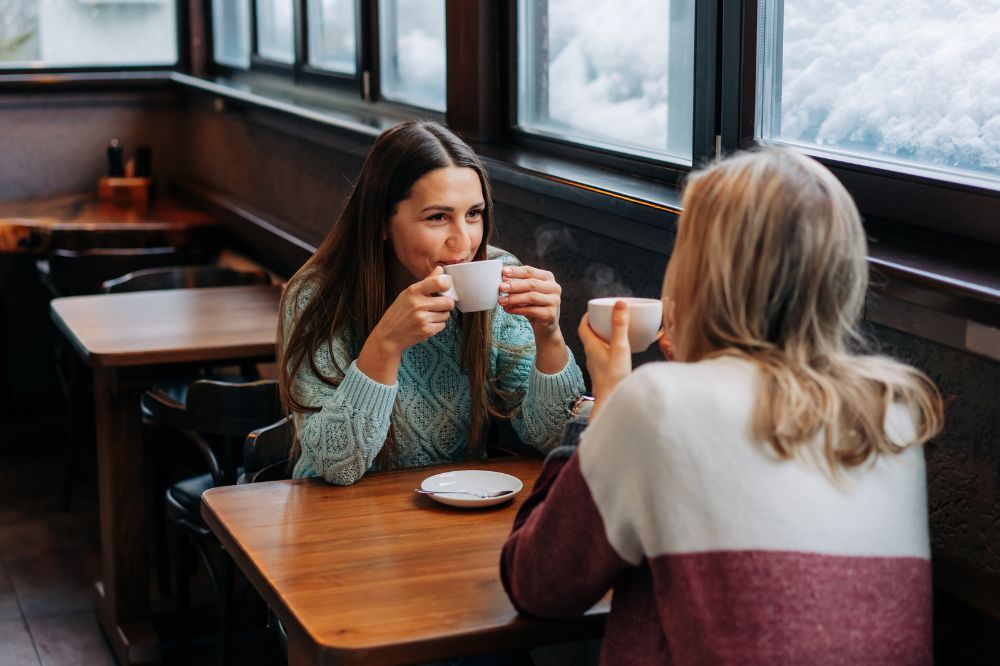 Dve ženy sedia za stolom pri káve a rozprávajú sa, čo je ďalším spôsobom ako zatočiť so stresom.
