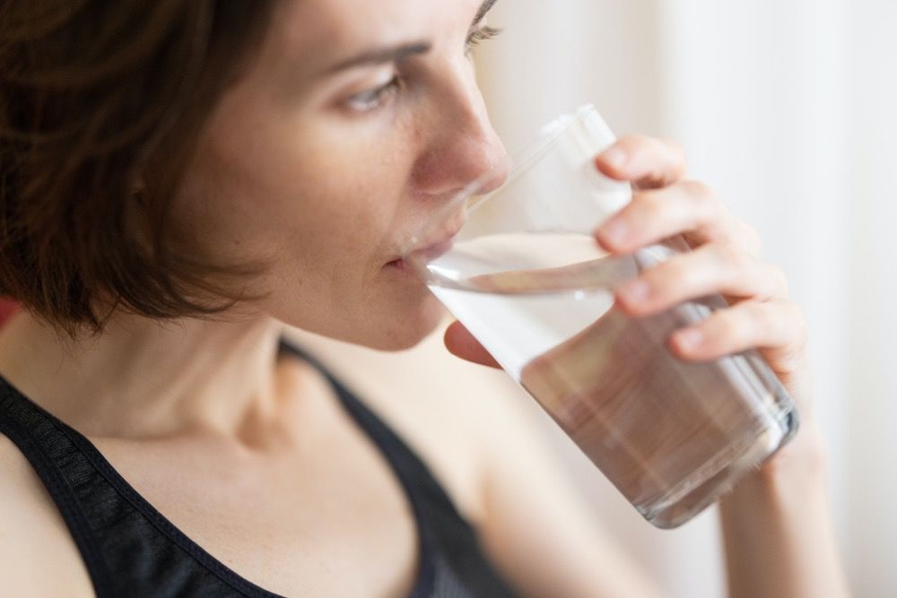 Draslík - správna hydratácia organizmu. Žena v čiernom tielku pije vodu z skleného pohára.