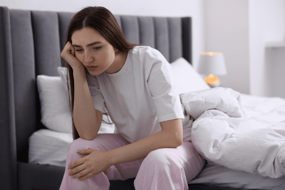 Žena sedí na posteli a je veľmi unavená, pretože trpí anémiou, ktorá je aj dôsledkom deficitu kyseliny listovej.