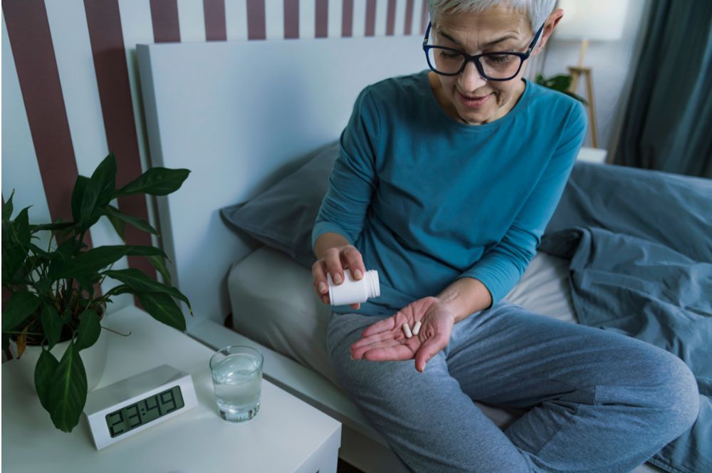 Staršia žena si do ruky sype dve tabletky s melatonínom, pretože starší ľudia majú menej melatonínu a trpia nespavosťou, preto si musia melatonín dopĺňať.