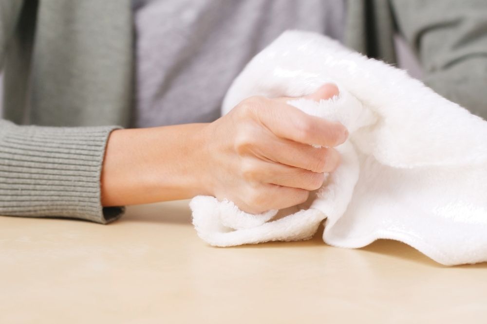 Žena sedí za stolom a drží v ruke uterák.
