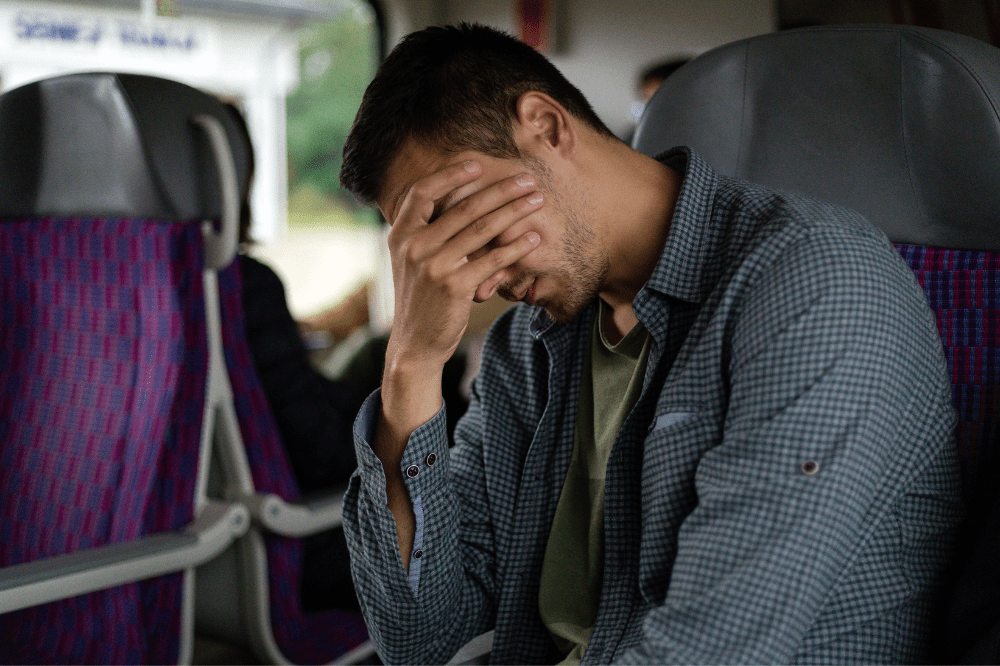 Muž sedí vo vlaku a drží sa za hlavu, pretože pociťuje silnú nevoľnosť kvôli cestovaniu.
