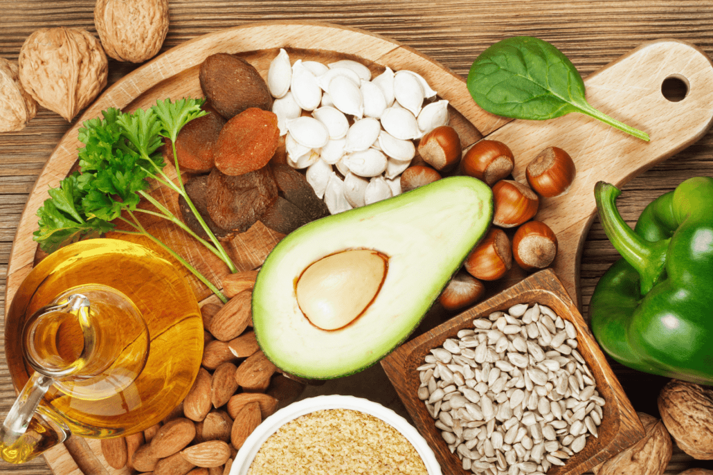Na drevenej doske sú položené potraviny s vitamínom E: avokádo, oleje, orechy, semienka.