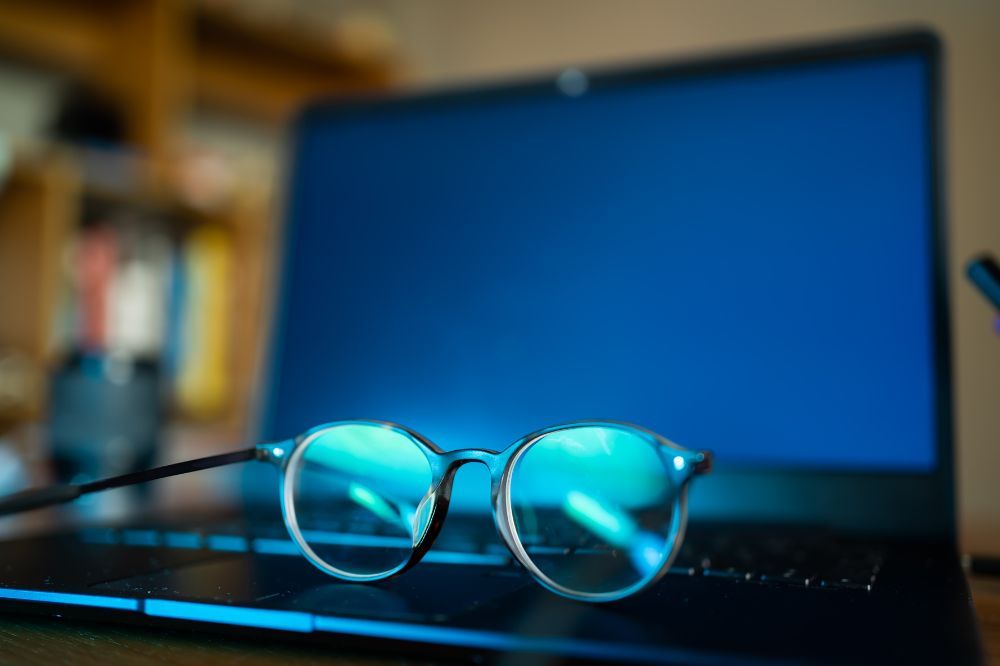 Na notebooku ležia okuliare s filtrom modrého svetla, ktoré sú navrhnuté na blokovanie významnej časti modrého svetla.