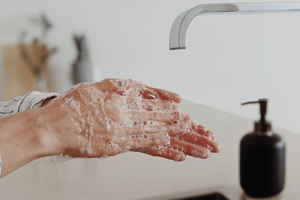Namydlené ruky pod kohútikom na vodu, predstavujú umývanie rúk a správnu hygienu, ktoré predstavujú prevenciu pred prenosom baktérií.