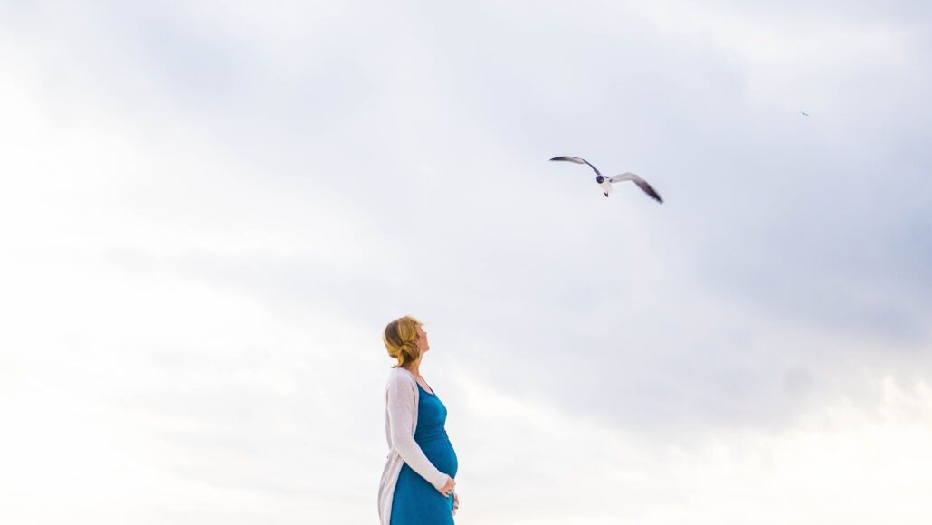 Tehotná žena v modrých šatách je na prechádzke, pretože pohyb je skvelým spôsobom odbúravania cukru v krvi a znižuje riziko tehotenskej cukrovky.