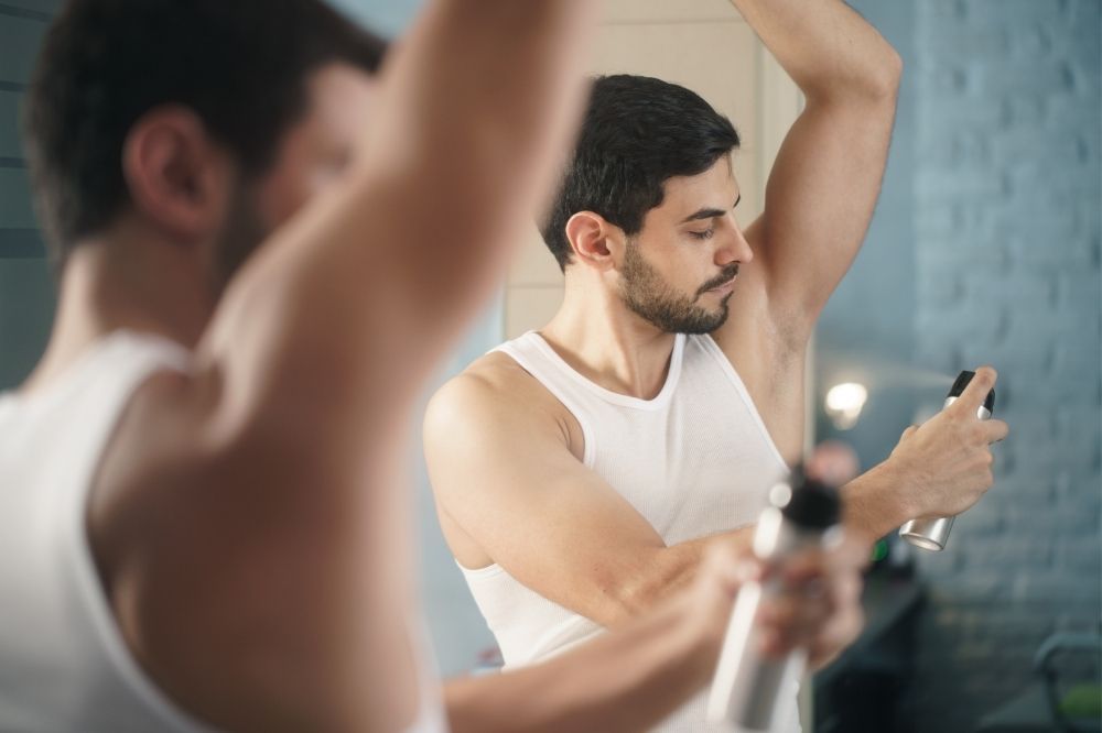 Muž pred zrkadlom si aplikuje antiperspirant.