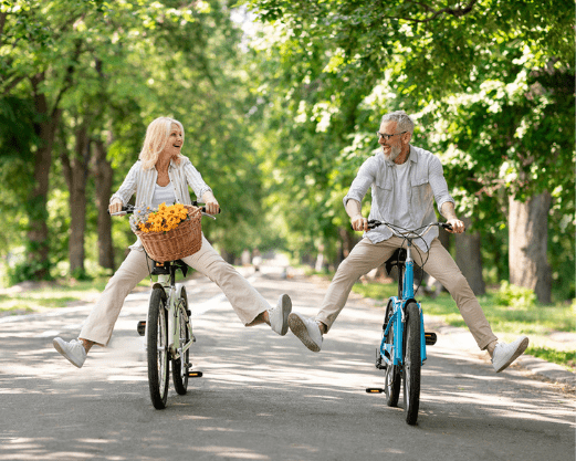 Šťastný starší pár si užíva aktívny cyklistický výlet v parku – ideálne s GS Extra strong multivitamín 50+.