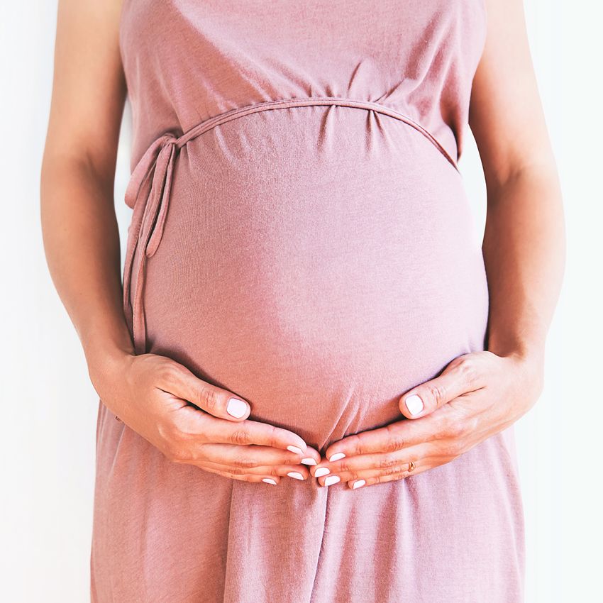 Tehotná žena v ružových šatách si drží svoje tehotenské bruško a zvažuje príjem Omega-3 mastných kyselín, ktoré sú tomto období veľmi dôležité pre správny vývoj bábätka.