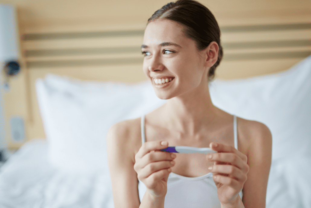 Žena sa pozerá na tehotenský test a usmieva sa pretože je tehotná.